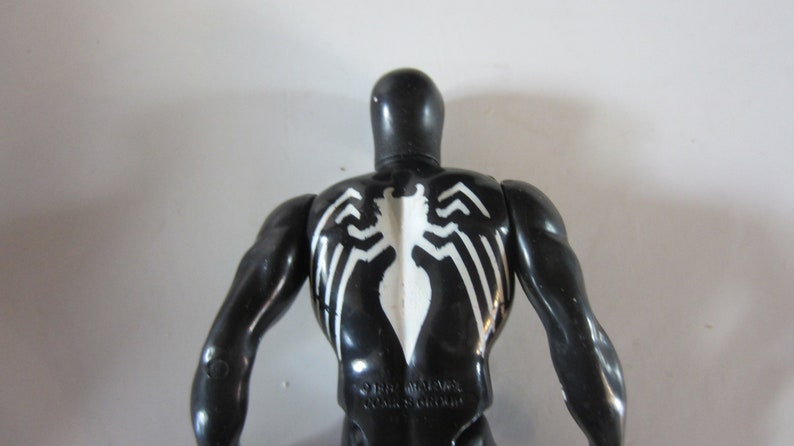 May include: Black action figure of a superhero with a white spider emblem on the back. The figure has a glossy finish and muscular arms. The figure is a collectible toy.