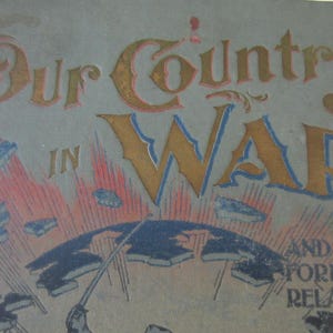 May include: Vintage book titled "Our Country in War and Our Foreign Relations." The cover is a muted blue-gray with gold and blue lettering. The illustration depicts a globe with radiating lines and falling objects.