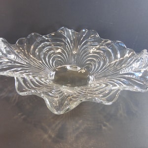 May include: Clear glass decorative bowl with a scalloped edge and a central, shallow depression. The bowl features a radiating, textured pattern, creating a visual effect reminiscent of a flower or shell. The glass is transparent, allowing light to pass through.