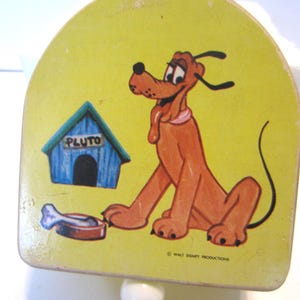 May include: A vintage Pluto toy featuring a yellow background with a cartoon Pluto, a blue dog house with "PLUTO" on it, and a bone. The toy has a white ball at the bottom and is marked "WALT DISNEY PRODUCTIONS".