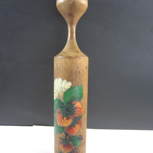 May include: A wooden muddler with a bulbous top and a cylindrical body. The body is decorated with a hand-painted design of strawberries and a white flower with green leaves. The muddler is made of light brown wood.