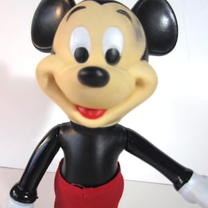 Pode incluir: Uma figura vintage do Mickey Mouse com corpo preto, cal&ccedil;&otilde;es vermelhos e luvas brancas. A figura tem um rosto bege com orelhas, olhos e boca vermelhos. Bra&ccedil;os e pernas articulados.
