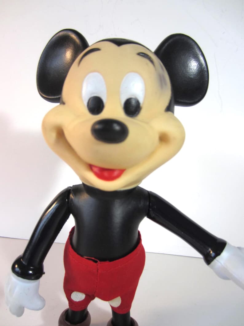 Pode incluir: Uma figura vintage do Mickey Mouse com corpo preto, cal&ccedil;&otilde;es vermelhos e luvas brancas. A figura tem um rosto bege com orelhas, olhos e boca vermelhos. Bra&ccedil;os e pernas articulados.