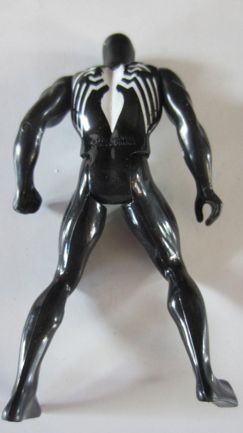 May include: Black action figure of a superhero with white spider-web-like markings on the chest and back. The figure has a muscular build and is posed with legs apart and arms slightly outstretched. The figure is made of a glossy plastic material.
