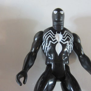 May include: A black action figure of a superhero with a white spider emblem on the chest. The figure has a black head with white eye shapes and white spider web designs on the chest and back.