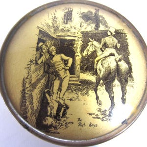 May include: A round, antique metal container with a detailed black and white illustration. The image depicts a scene with figures, a horse, and a building, with the text "The Post Boys" at the bottom. The container has a gold-toned interior and a silver-colored rim.