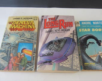 May include: Three vintage science fiction books. Titles include "The Genesis Machine" by James P. Hogan, "The Long Run" by Daniel Keys Moran, and "Star Born" by Andre Norton. Each book features colorful cover art with futuristic themes.