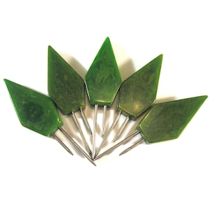 May include: Five vintage green art deco style hat pins arranged in a fan shape. Each pin features a diamond-shaped, marbled green head and a silver-colored metal pin.