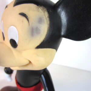 Pode incluir: Uma figura vintage do Mickey Mouse. A figura tem uma cabe&ccedil;a preta com grandes orelhas pretas, um rosto cor de creme e cal&ccedil;&otilde;es vermelhos. A figura est&aacute; em posi&ccedil;&atilde;o de andar.