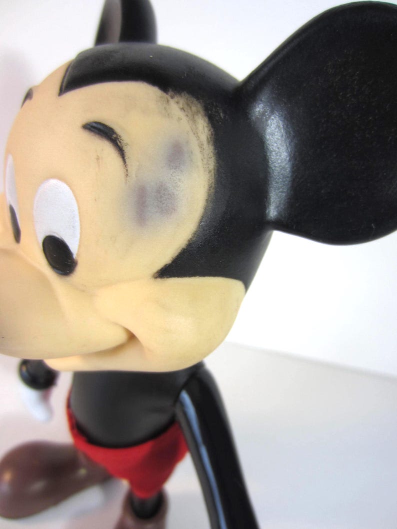 Pode incluir: Uma figura vintage do Mickey Mouse. A figura tem uma cabe&ccedil;a preta com grandes orelhas pretas, um rosto cor de creme e cal&ccedil;&otilde;es vermelhos. A figura est&aacute; em posi&ccedil;&atilde;o de andar.