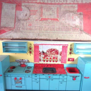 May include: Vintage toy kitchen set with a red and white box on top. The kitchen is light blue with red and yellow accents. It features a stove, sink, and refrigerator. The kitchen set has a retro design.