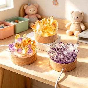 May include: Three circular wooden base lamps topped with clusters of raw crystals. One lamp features yellow citrine, one features purple amethyst, and one features a mix of yellow citrine and purple amethyst. Each lamp has a white power cord.