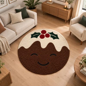 May include: A round, textured area rug shaped like a Christmas pudding. The rug features a dark brown base with a cream-colored top, decorated with three red berries and two green holly leaves. A simple, dark curved line forms a smiling face.