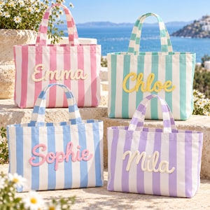May include: Four rectangular canvas tote bags with vertical stripes in pink, teal, light blue, and purple. Each bag features two handles and a personalized name in cursive script: Emma in cream, Chloe in yellow, Sophie in pink, and Mila in cream.