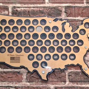 Pode incluir: Um mapa de madeira de cor clara dos Estados Unidos com recortes circulares para uma coleção de moedas. O mapa inclui o texto 50 State Quarters e uma pequena bandeira americana. É fixado com parafusos prateados nos cantos.