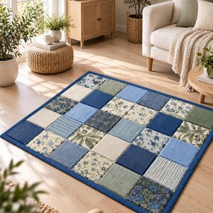 May include: A rectangular area rug featuring a patchwork design of square tiles in various shades of blue, cream, and sage green. The pattern includes solid colors, floral prints, and striped textures, all bordered by a solid dark blue fabric edge.