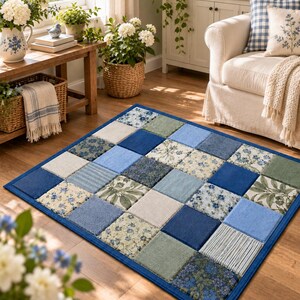 May include: A rectangular area rug featuring a patchwork design of square tiles in various shades of blue, green, and cream. The pattern includes solid colors, floral prints, and striped textures, all bordered by a solid dark blue fabric trim.