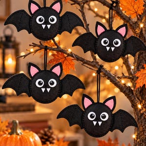 May include: Four black felt bat ornaments with pink inner ears, large white eyes with black pupils, and two white fangs. Each bat has a circular body, outstretched wings, and a black string loop attached to the top for hanging purposes.
