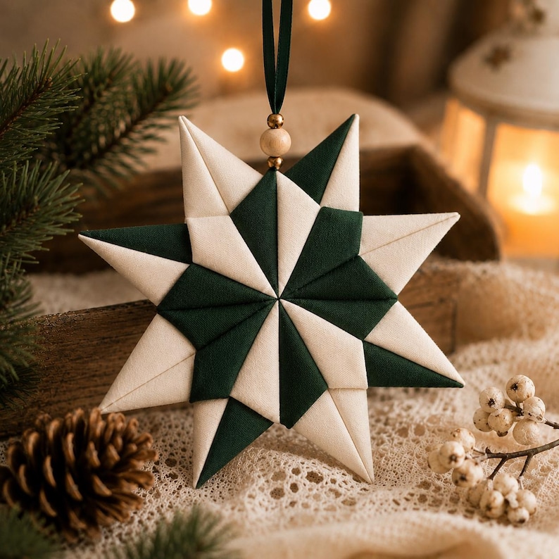 May include: A star-shaped fabric ornament featuring a geometric pattern of alternating dark forest green and cream-colored fabric segments. The ornament is suspended by a dark green ribbon accented with a single small wooden bead at the top.