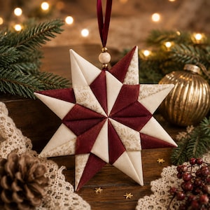 May include: A quilted star-shaped ornament featuring alternating points of solid deep burgundy fabric and cream fabric with a subtle gold botanical print. The ornament hangs from a dark red ribbon with a single wooden bead at the top center.