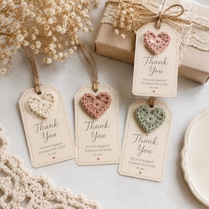Op de afbeelding: Vier rechthoekige papieren cadeaulabels met afgeronde hoeken, elk voorzien van een gehaakt hartje in crème, oudroze of saliegroen. De labels zijn bedrukt met de tekst Thank You for your support! It means the world to me. en zijn voorzien van touw.