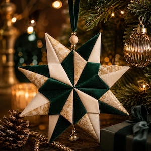 May include: A multi-pointed star ornament constructed from fabric panels in dark green velvet, cream-colored fabric, and gold-patterned fabric. The star features a green velvet ribbon loop at the top with a wooden bead and a small gold bell at the bottom.