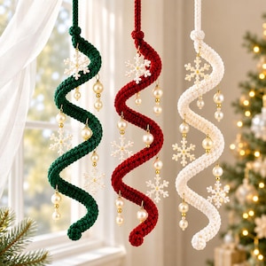 May include: Three spiral hanging ornaments in dark green, deep red, and cream white. Each twisted cord features dangling white snowflake charms and lustrous cream-colored pearl beads attached with small gold-toned metal rings and hooks.