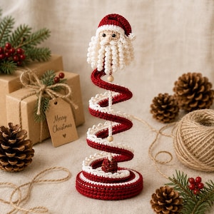 Puede incluir: Una figura de Pap&aacute; Noel tejida a ganchillo sobre una base en espiral roja y blanca. El Pap&aacute; Noel tiene un gorro rojo, una barba blanca y ojos negros. La estructura en espiral se apoya en un poste central con peque&ntilde;as cuentas de madera.
