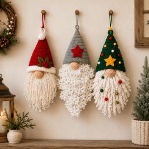 Pode incluir: Tr&ecirc;s ornamentos suspensos de gnomos em croch&ecirc; com gorros pontiagudos. O gnomo da esquerda tem um gorro vermelho com azevinho, o central um gorro cinza com uma estrela vermelha e o da direita um gorro verde com uma estrela amarela e pompons.