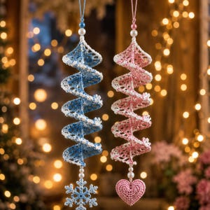 May include: Two hanging spiral ornaments made of crocheted thread. One is blue and white with a snowflake charm at the bottom, and the other is pink and white with a heart charm at the bottom. Both feature small white and colored beads at the top.