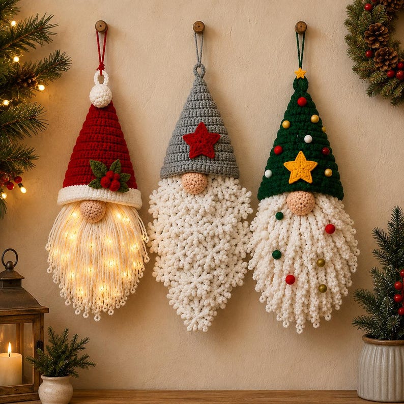 Pode incluir: Tr&ecirc;s ornamentos de gnomos de croch&ecirc; pendurados com chap&eacute;us pontiagudos. O gnomo da esquerda tem um chap&eacute;u vermelho com azevinho, o do centro um chap&eacute;u cinza com uma estrela vermelha e o da direita um chap&eacute;u verde com uma estrela amarela.