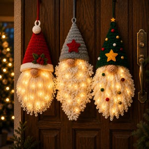 Pode incluir: Tr&ecirc;s decora&ccedil;&otilde;es suspensas de gnomos feitas de fio de croch&ecirc;. O gnomo da esquerda tem um gorro vermelho com azevinho, o central um cinza com uma estrela vermelha e o da direita um verde com uma estrela amarela. Cada barba branca integra luzes LED.
