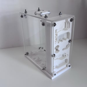 Peut inclure: Un fourmilière verticale composée de panneaux en acrylique transparent et d'une structure intérieure blanche imprimée en 3D avec des tunnels et des chambres complexes. L'unité est assemblée par des vis et des écrous métalliques.