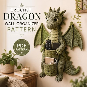Op de afbeelding: Een groene gehaakte draak als wandorganizer met grote vleugels en een buidel op de buik met daarin een afstandsbediening, een smartphone, een klein notitieboekje en witte bedrade oordopjes. De tekst luidt CROCHET DRAGON WALL ORGANIZER PATTERN.