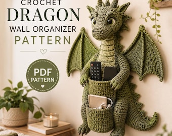 May include: A green crochet dragon wall organizer with large wings and a pouch on its belly holding a remote control, a smartphone, a small notebook, and white wired earbuds. The text reads CROCHET DRAGON WALL ORGANIZER PATTERN and PDF PATTERN.