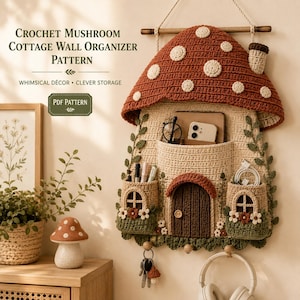 Puede incluir: Un organizador de pared de ganchillo con forma de seta, con un gran sombrero rojo de puntos blancos, cuerpo beige con dos bolsillos laterales, puerta central y tres ganchos. El texto dice Crochet Mushroom Cottage Wall Organizer Pattern.