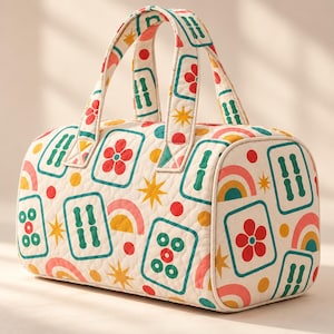 May include: A quilted duffel bag featuring an off-white base with a repeating pattern of mahjong tiles, red flowers, yellow stars, and colorful rainbows. The bag has two top handles and a rectangular shape with rounded edges.