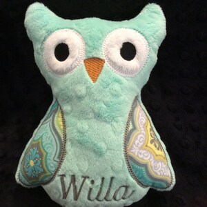 May include: A teal blue plush owl with embroidered eyes and a beak. The owl has a patterned fabric on the wings and the name "Willa" embroidered on the front.