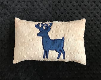 May include: A white plush pillow with a blue embroidered deer design. The pillow has a textured surface.