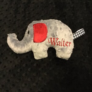 May include: A gray plush elephant toy with a red letter D on its side and the name Walter embroidered on its body. The elephant has a black and white checkered tail.