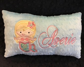 May include: A light blue pillow with a pink and green embroidered mermaid and the name "Aerie" in pink cursive.