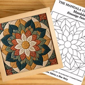 May include: A square Kinusaiga fabric art piece in a light wood frame featuring a floral mandala design in teal, mustard yellow, and rust orange, accompanied by a printed paper pattern titled THE MANDALA COLLECTION Mandala Kinusaiga Pattern.