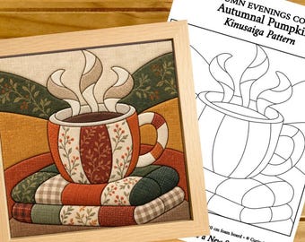 Puede incluir: Una pieza de arte en tela Kinusaiga enmarcada que representa una taza humeante sobre una pila de mantas, acompañada de una hoja de patrón impresa titulada Cosy Autumn Evenings Collection Autumnal Pumpkin Kinusaiga Pattern con ilustraciones de líneas negras.