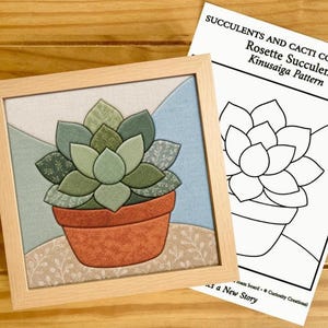 Peut inclure: Un cadre carré en bois clair contenant une œuvre en tissu Kinusaiga représentant une plante succulente verte dans un pot en terre cuite, accompagnée d'une fiche d'instructions blanche intitulée SUCCULENTS AND CACTI COLLECTION Rosette Succulent Kinusaiga Pattern.