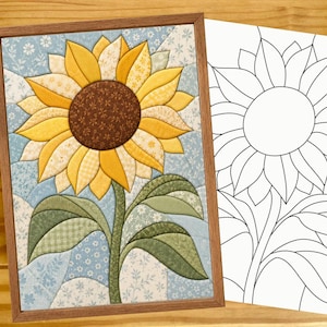 May include: A framed fabric sunflower quilt block featuring yellow and gold petals, a dark brown center, and green leaves against a light blue floral background, displayed alongside a matching black and white line art pattern template.