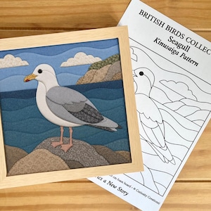 Peut inclure: Une œuvre d'art en tissu Kinusaiga encadrée représentant un goéland debout sur un rocher au bord de la mer, accompagnée d'un patron en papier intitulé British Birds Collection Seagull Kinusaiga Pattern avec le dessin au trait de l'oiseau.