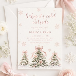 Um convite para chá de bebê com o texto baby it's cold outside em letra cursiva de ouro rosa. O design inclui três árvores de Natal ilustradas decoradas com laços e enfeites cor-de-rosa, rodeadas por flocos de neve.