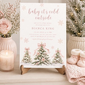 K&ouml;nnte beinhalten: Eine rechteckige Einladungskarte f&uuml;r eine Babyparty mit dem Text 'baby it's cold outside' in rosa Schreibschrift, illustriert mit drei verschneiten Weihnachtsb&auml;umen, die mit rosa Schleifen und Kugeln geschm&uuml;ckt sind, sowie Schneeflocken.