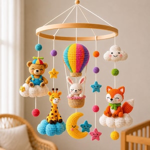 Op de afbeelding: Een hangende babymobiel met gehaakte figuren aan een rond houten frame. De figuren bestaan uit een beer op een wolk, een giraf op een blauwe wolk, een konijn in een regenboogkleurige luchtballon, een vos op een wolk en een gele halve maan.