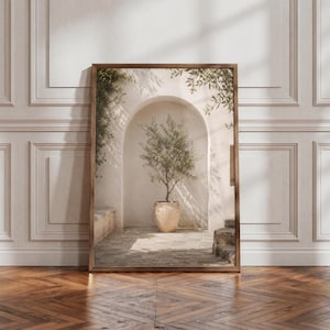Könnte beinhalten: Ein gerahmter vertikaler Wandkunstdruck mit einem Olivenbaum im Topf, der in einem Steinbogen zentriert ist. Die Szene zeigt einen hellen Steinboden, eine strukturierte Wand und weiche Schatten durch das Laub, alles in einem dunkelbraunen Holzrahmen.